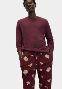 Camisa de manga larga burdeos combinada con joggers burdeos que presentan patrones de temática navideña en beige, incluyendo estrellas, hombres de jengibre y bastones de caramelo.
