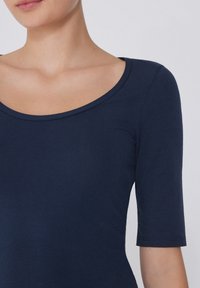 Námořnická modrá, přiléhavá halenka s krátkými rukávy a širokým kulatým výstřihem. Hladká, elastická tkanina s čistým, jednoduchým designem.