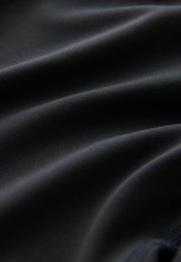 Czarna tkanina o gładkiej, satynowej fakturze. Powierzchnia ma delikatne fale i fałdy, co wskazuje na elastyczność i miękkość.