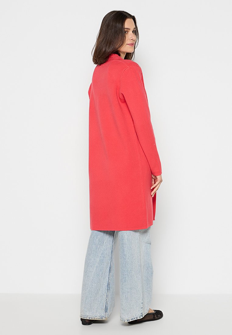 Langer, locker sitzender korallenfarbener Cardigan aus weichem Material, mit einem schlichten Design, langen Ärmeln und seitlichen Schlitzen am Saum.