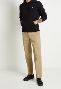 Felpa nera con cappuccio e tasca frontale, abbinata a chinos beige e sneakers nere. Design casual; tessuto leggero e vestibilità standard.