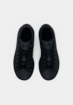 Coppia di sneakers nere basse con lacci, viste dall'alto, con finitura liscia effetto pelle e dettagli traforati sottili.