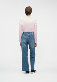 Svetlo roza pulover z udobnim krojem in odrezanim hrbtom, v kombinaciji s klasičnimi modrimi širokimi trapericami z visokim pasom in črnimi športnimi copati.