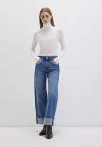 Weißes langärmliges Rollkragenoberteil, kombiniert mit hochtaillierten, weit geschnittenen blauen Jeans mit umgeschlagenem Saum und schwarzen Ankle Boots.