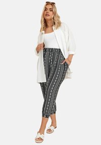 Pantalones recortados de patrón en blanco y negro, tejido suave, con cintura elástica, combinados con una blusa blanca ajustada y una camisa blanca suelta.