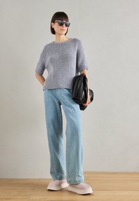 Lichtgrijze gebreide trui met korte mouwen, relaxte blauwe jeans, roze platform sneakers en een zwarte plissé handtas; zonnebril maakt de look compleet.
