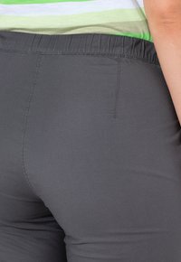 Grijze elastische taillebandbroeken met een soepele textuur, voorzien van een achterzaknaad en een getailleerde pasvorm. Het materiaal lijkt lichtgewicht en flexibel.