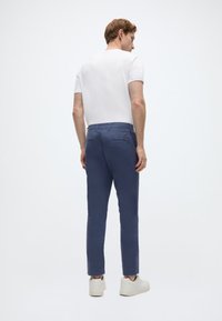 Κομψά navy chinos εφαρμοστής γραμμής από ελαφρύ ύφασμα, με τσέπες στο πίσω μέρος και κανονική ζώνη μέσης, σε συνδυασμό με λευκό απλό t-shirt και λευκά αθλητικά παπούτσια.