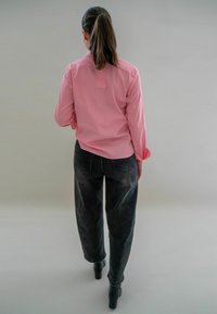 Roze lange mouwen shirt en donkergrijze broek, met een gladde stofstructuur. Hoge hakken complementeren de outfit.