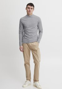 Camisa gris de manga larga con cuello alto, combinada con pantalones beige y zapatillas blancas. La tela parece suave y ajustada.