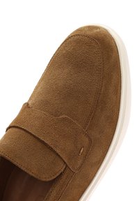 Brown suede slip-on shoe with a round toe, feature a wide strap across the upper and a white rubber sole. Soft texture and minimal stitching details.
