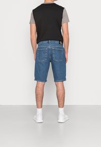Denim shorts in blue with a relaxed fit, five-pocket design, and rolled hems. Paired with a black and gray short-sleeve t-shirt. White sneakers.