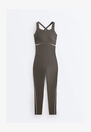 Bezruký priliehavý overal v olivovo zelenej farbe s prekríženými ramienkami na chrbte, výrezmi vpredu pod prsiami a úzkymi nohavicami so svetlými detailmi po stranách.