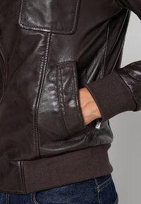 Braune Lederjacke mit glatter Textur, gerippten Bündchen und einer Seitentasche. Hat ein tailliertes Design mit minimalen Nähdetails.