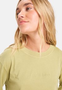 T-shirt verde chiaro a maniche lunghe con scollatura rotonda e logo ricamato "Quiksilver". Tessuto morbido con una texture liscia.
