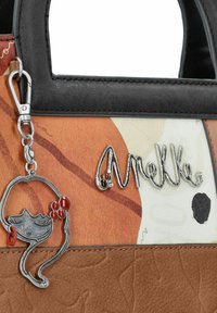 Sac marron et orange avec des accents noirs, arborant un charm en argent en forme de chat intriqué et le nom de la marque en script argenté. Surfaces texturées.
