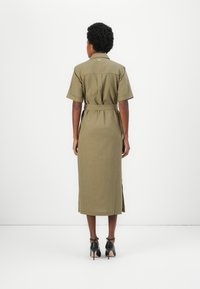 Καφέ λινό midi φόρεμα με κοντά μανίκια, ζώνη που δένει στη μέση, πλαϊνές σχισμές και γιακά. Φορεμένο με μαύρες ψηλοτάκουνες γόβες.