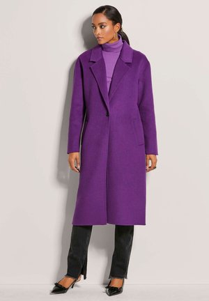Long purple coat with a notched collar, single button closure, and side pockets. Worn over a light purple turtleneck and black jeans.
