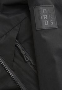 Svart ytterjacka med texturerad patch med "COLOR KIDS"-logotyp, dragkedjestängning och slät foder synligt.
