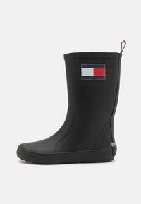 Botte de pluie en caoutchouc noir avec une finition lisse, présente un logo de drapeau coloré sur le côté et une semelle texturée pour une meilleure adhérence.