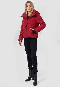 Red puffer jacket with a hood, featuring a zippered front and black accents, paired with black fitted pants and ankle boots. Smooth texture.