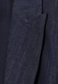 Tissu texturé bleu foncé avec un motif de tissage diagonal visible et un pli ou une couture triangulaire distincte.