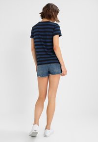 Camiseta de rayas en azul marino y azul oscuro, de mangas cortas, combinada con pantalones cortos de mezclilla. Zapatillas blancas completan el look casual.