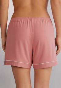 Ljusrosa shorts med elastisk midja och vikt kant. Funktioner en tunn vit detalj längs botten. Mjukt, andningsbart tyg.