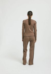 Brauner Langarmoberteil und passende Hose. Gerippte Textur mit schwarzen seitlichen Streifen. Der Oberteil hat einen gewellten Saum und eine Borte.