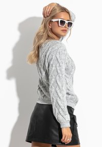 Jasnoszara sweter o splocie warkoczowym z okrągłym dekoltem, zestawiony z czarną skórzaną mini spódnicą. Całość uzupełniają okrągłe białe okulary przeciwsłoneczne.