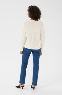 Cream-colored knit sweater with a ribbed hem and cuffs, paired with blue straight-leg jeans and black heeled mules.