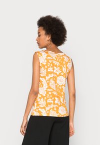 Top laranja sem mangas com padrões florais brancos, decote redondo e design ajustado. O material parece suave com uma textura lisa.