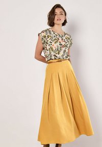 Top de estampado floral con mangas cortas, combinado con una falda maxi amarilla de cintura alta y plisada, que cuenta con un cinturón a juego y una textura suave.