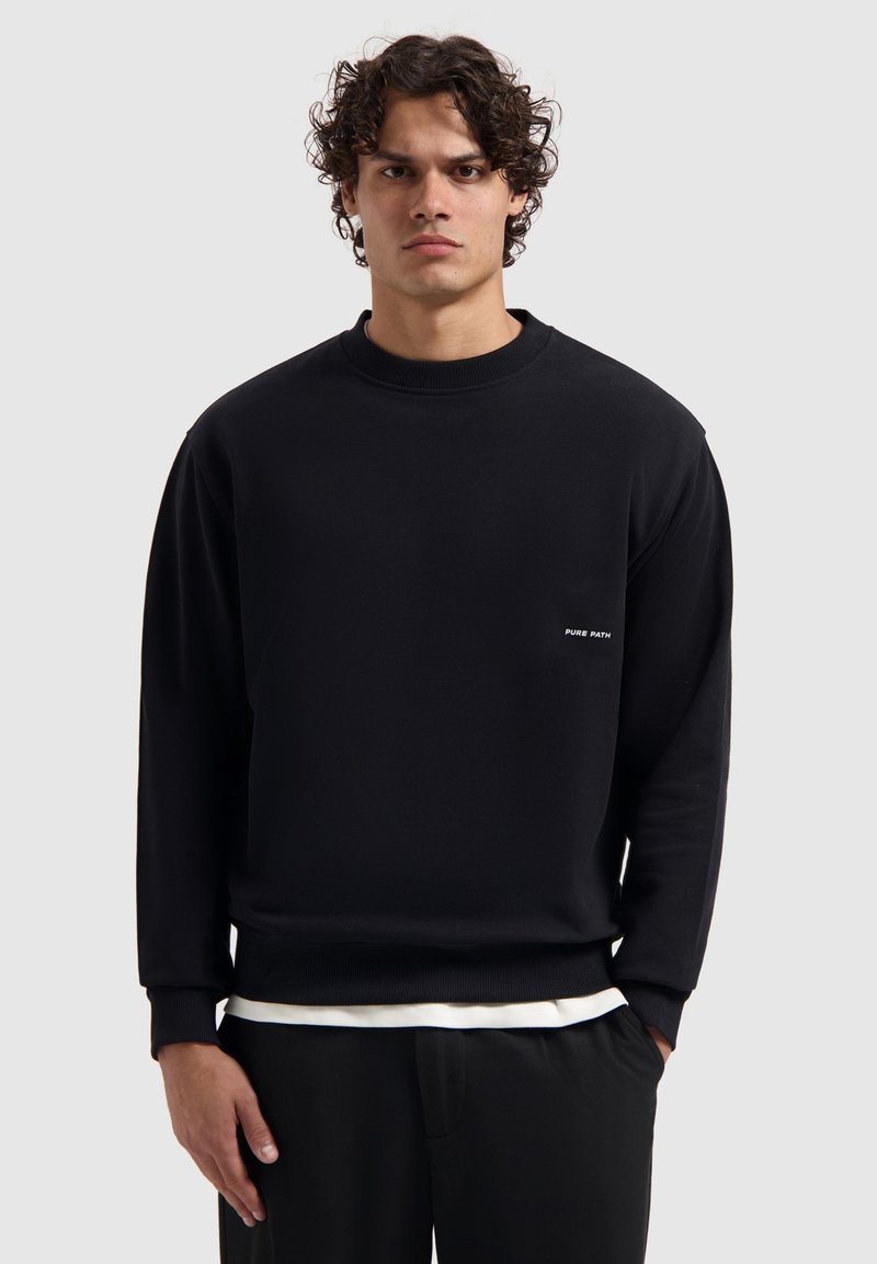 Zwarte sweatshirt in een losse pasvorm met een ronde hals. Bevat een klein wit logo op de linkerkant van de borst en ribgebreide boorden en zoom.