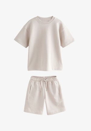 Béžový top s krátkym rukávom a okrúhlym výstrihom v páre s béžovými šortkami s elastickým pásom, ktoré majú predné vrecká a sťahovaciu šnúrku.