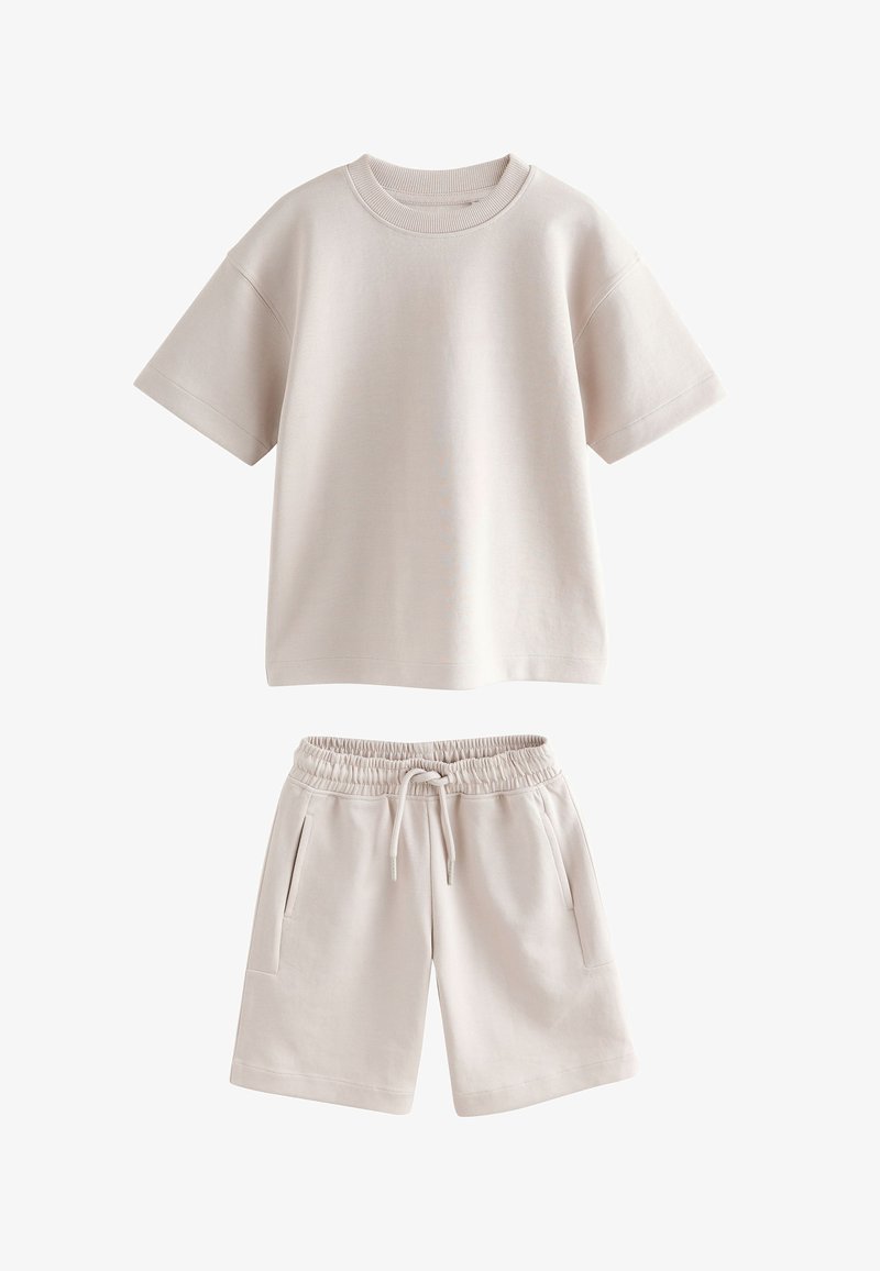 Béžový top s krátkym rukávom a okrúhlym výstrihom v páre s béžovými šortkami s elastickým pásom, ktoré majú predné vrecká a sťahovaciu šnúrku.