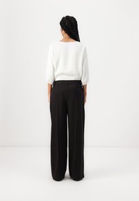 Blouse blanche à manches ballons associée à un pantalon noir ample. Tissu lisse avec un design épuré et une silhouette structurée.