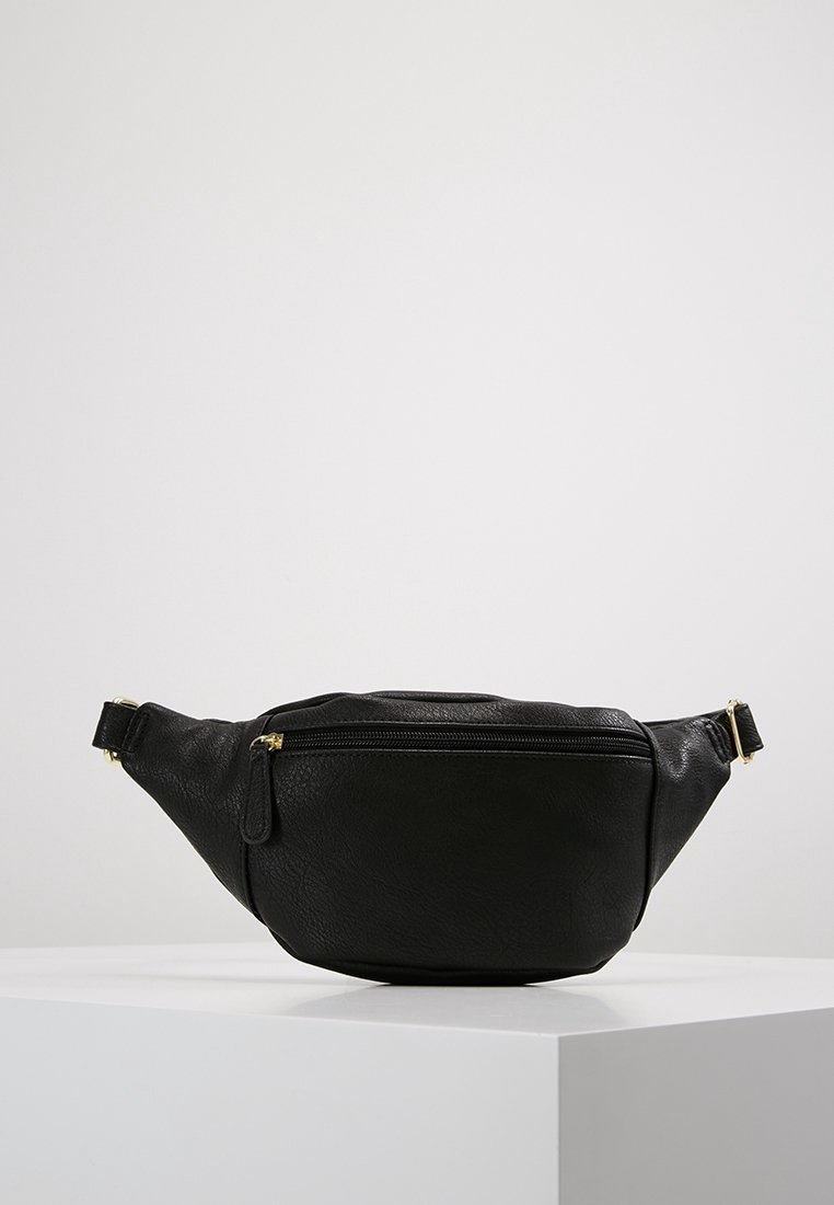 Sac banane en cuir noir avec fermeture éclair dorée et sangle réglable présenté sur un socle blanc devant un fond uni.