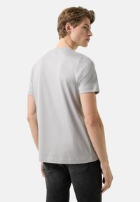 Lysegrå T-shirt med korte ærmer og rund halsudskæring, glat tekstur, kombineret med mørke jeans. Set bagfra.