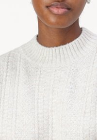 Lysfarget ribbestrikket genser med høy hals og teksturert stoff. Designet har et mykt, noe lodden utseende.