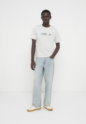 Grijs grafisch T-shirt met korte mouwen, voorzien van een ontwerp met meerkleurige tekst. Gecombineerd met lichtblauwe wijde jeans en witte sneakers.