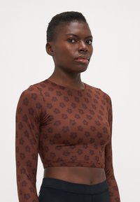 Brun langermet crop topp med et blomsterdesign i en mørkere nyanse, laget av et glatt og elastisk stoff.