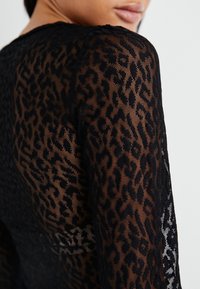Svart långärmad topp med ett genomskinligt spetsmaterial och ett leopardmönster. Designen har en texturerad yta längs ärmarna.