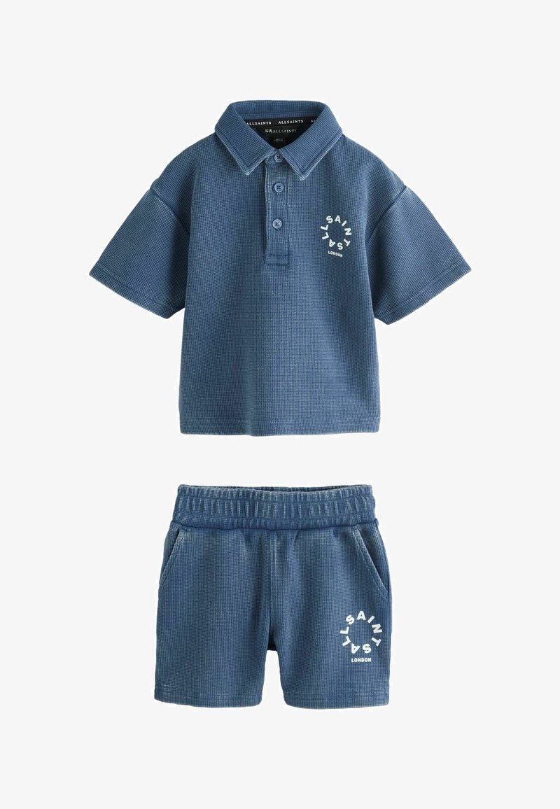 Sinine tekstuuriga lühikeste varrukatega polo-särk ja sobivad elastse vöökohaga püksid, millel on valge ümmargune "AllSaints London" logo rinnal ja säärel.
