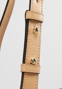 Cinghietto in pelle beige con accenti marroni scuri, dotato di parti in metallo color oro e cuciture ordinate, che presenta una texture liscia.