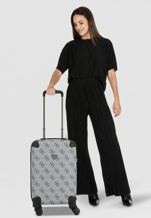 Maleta rígida con exterior gris con patrón, acentos negros, cuatro ruedas, mango retráctil y detalle de logo en la parte frontal.