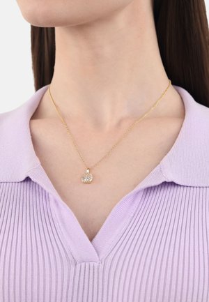 Collar de oro con un colgante cuadrado que presenta un racimo de cristales transparentes, llevado sobre una blusa de rayas en tono púrpura claro con escote en V.