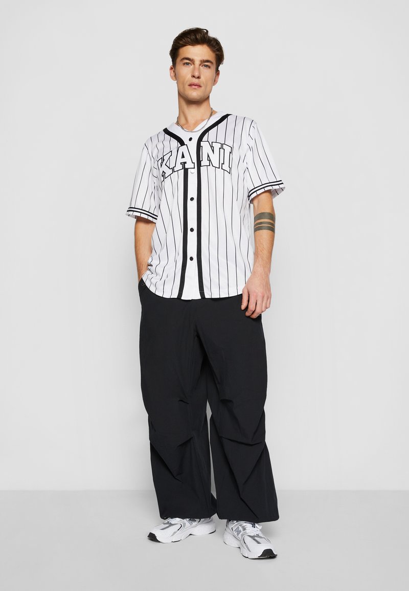 Homme en chemise de maillot de baseball blanc et noir et pantalon blanc