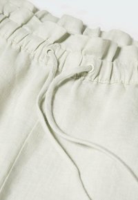 Short en tissu beige clair avec taille élastique et détail de cordon passant par des œillets métalliques.