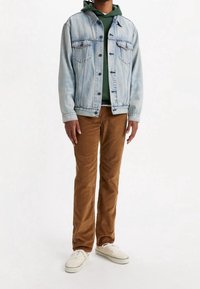 Jasnoniebieska kurtka dżinsowa na zielonej bluzie z kapturem, zestawiona z brązowymi spodniami sztruksowymi i białymi tenisówkami. Posiada zapięcie na guziki i boczne kieszenie.